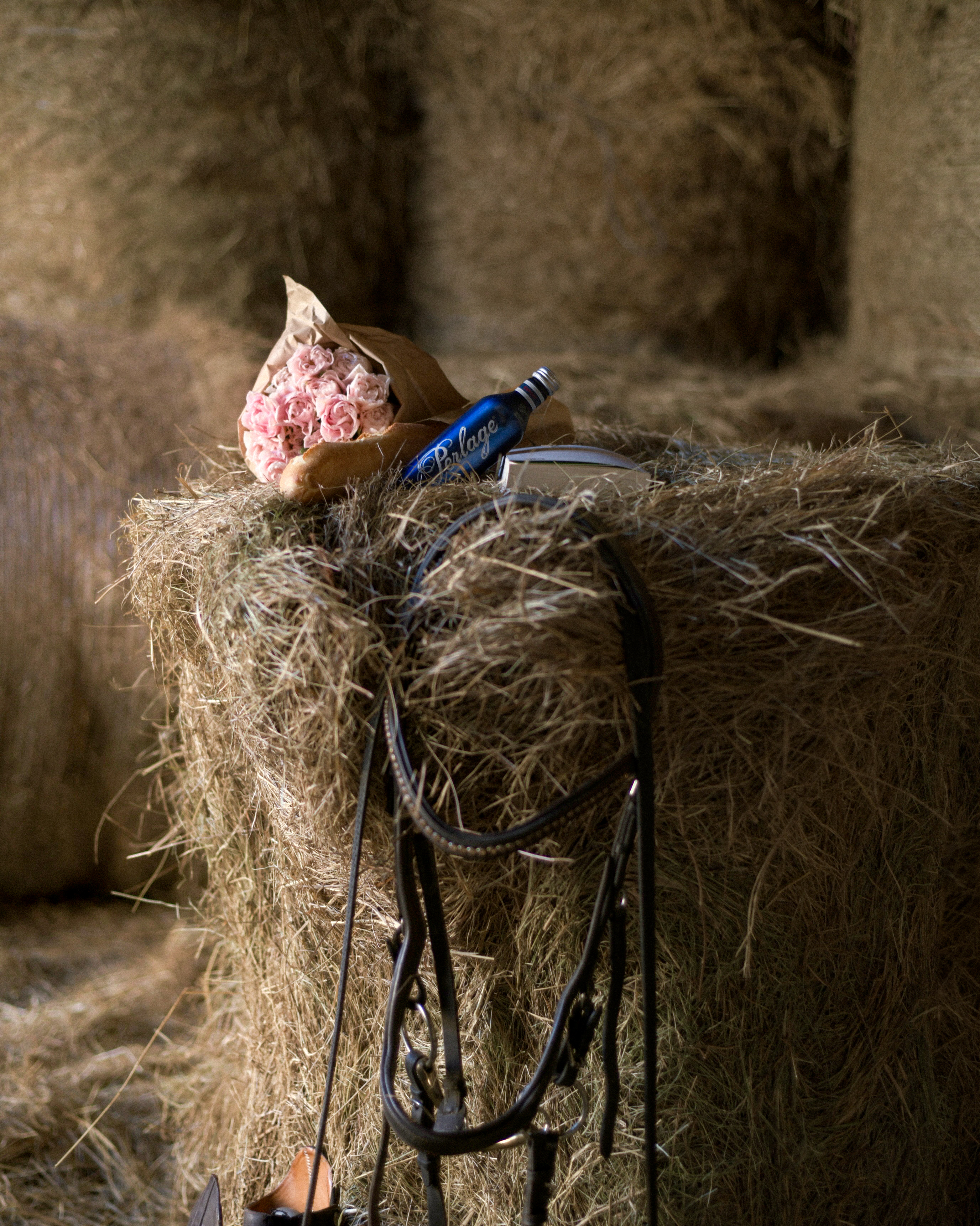 A PERLAGE bottle on hay with a bouquet of roses