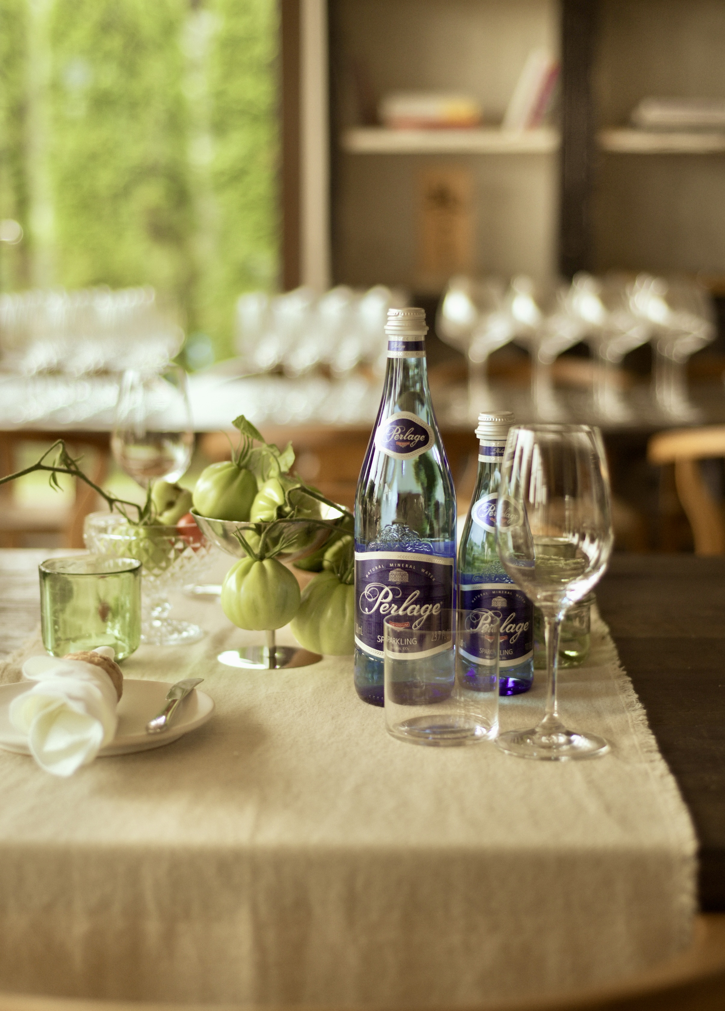 A PERLAGE bottle on a table with wine glasses and vegetables